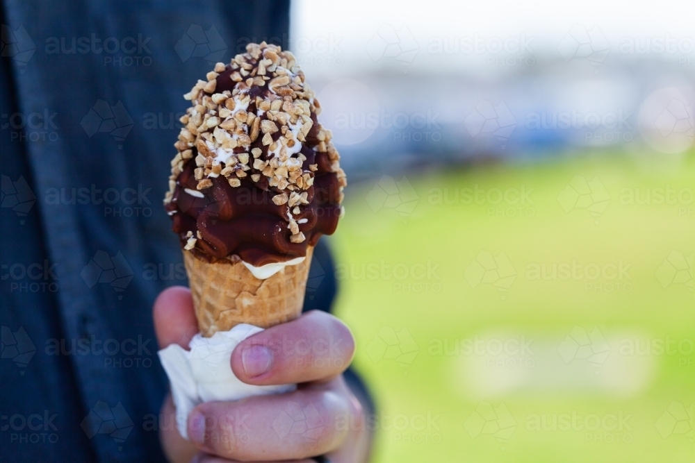 man holding soft serve ice cream with choc nut toping on sunny day - Australian Stock Image