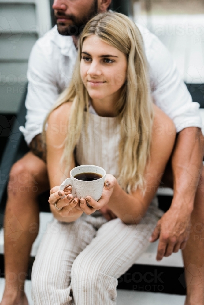 Man holding woman from behind as they sit on the steps of their porch - Australian Stock Image