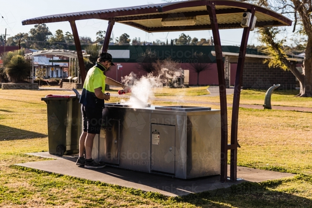 Man in hat cleaning hot barbecue with steam - Australian Stock Image