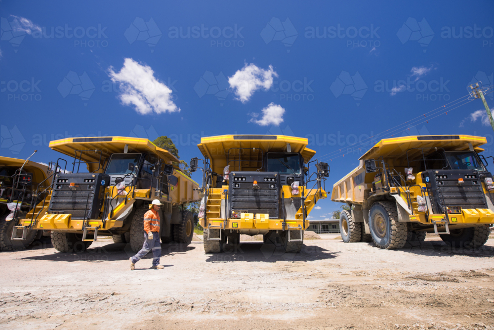 Man in high visibility clothing walking in front of haul trucks. - Australian Stock Image