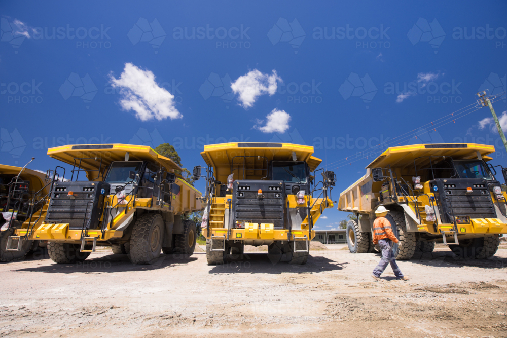 Man in high visibility clothing walking in front of haul trucks. - Australian Stock Image
