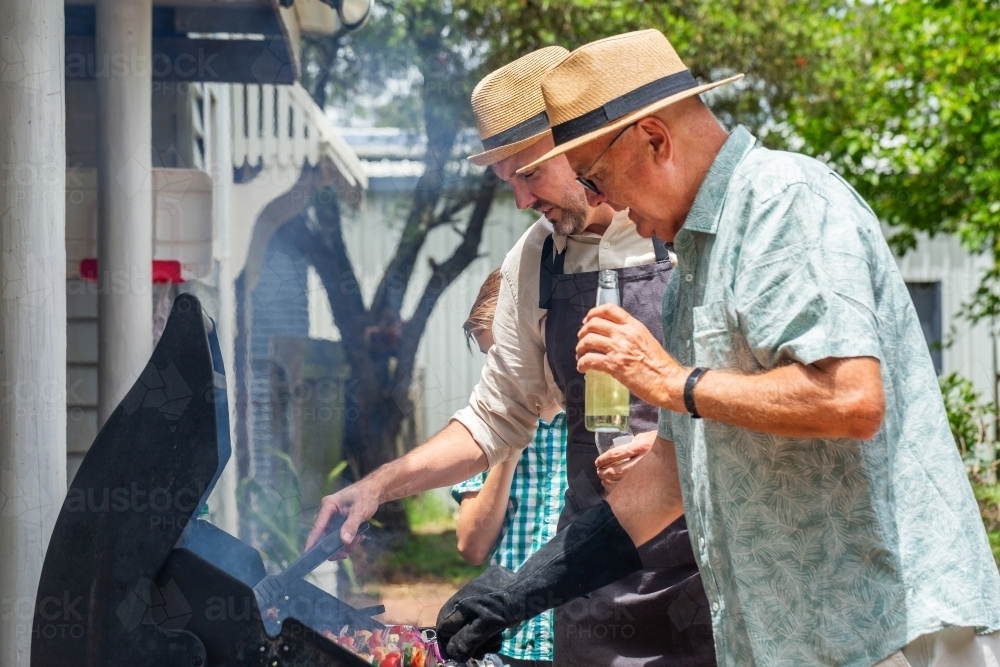 Man in his sixties drinking cider from bottle while standing by barbeque - Australian Stock Image