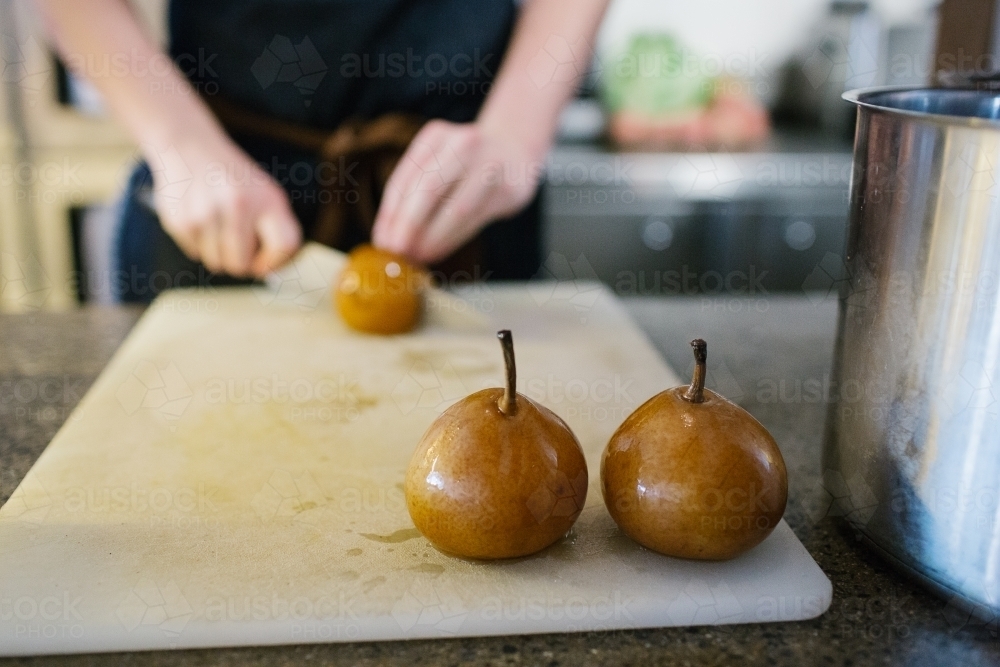 Man in kitchen slicing a cooked brown pear fruit - Australian Stock Image