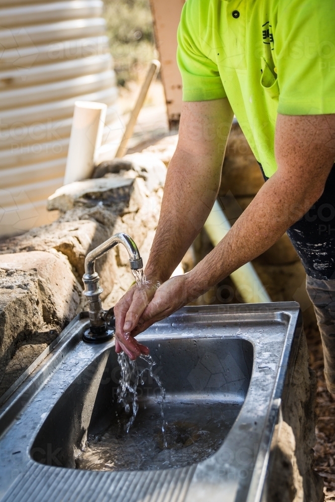 Man in yellow shirt washing hands at outdoor sink - Australian Stock Image