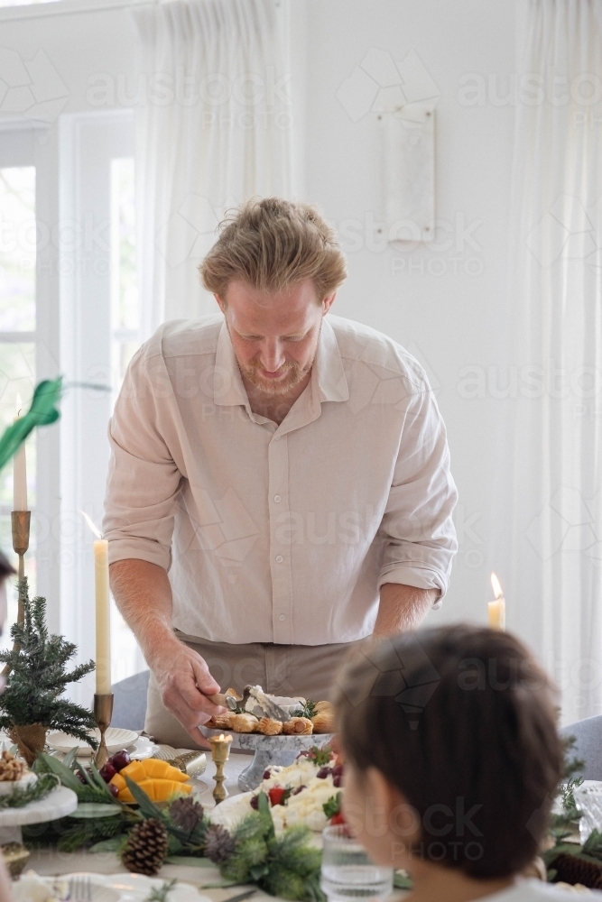 Man lighting serving up pavlova on dining table at Christmas - Australian Stock Image