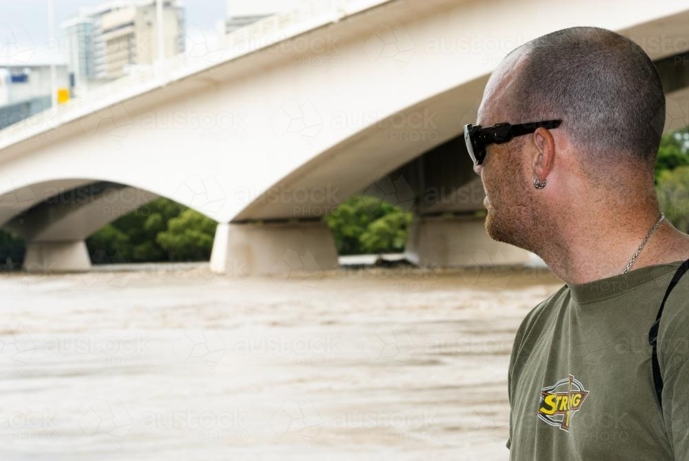 Man looking out on flooded Brisbane River with Captain Cook Bridge - Australian Stock Image