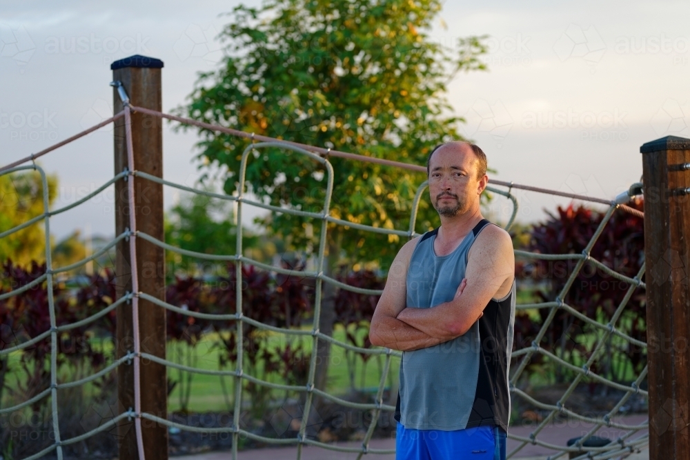 Man of mixed race standing with folded arms at sunset in a park - Australian Stock Image