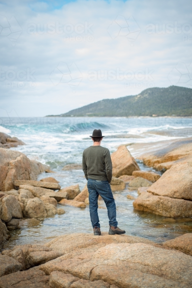 Man on boulder rocks at beach - Australian Stock Image