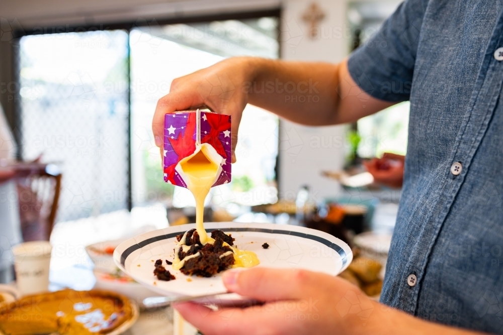 Man pouring custard onto traditional Christmas pudding - Australian Stock Image