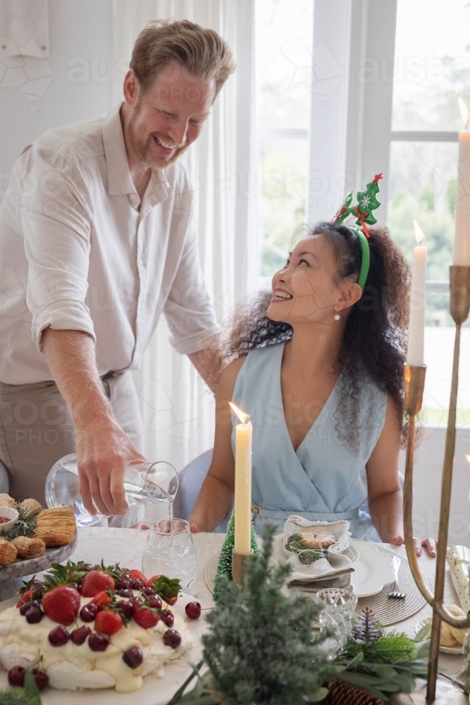 Man pouring water for his wife at Christmas table - Australian Stock Image