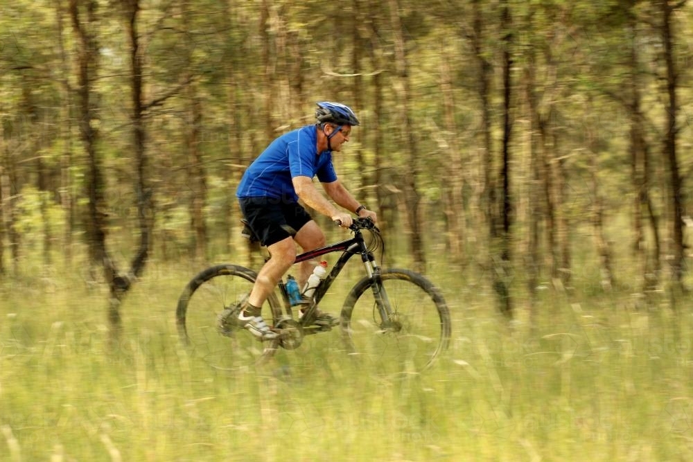 Man riding his pushbike on a dirt track among trees - Australian Stock Image