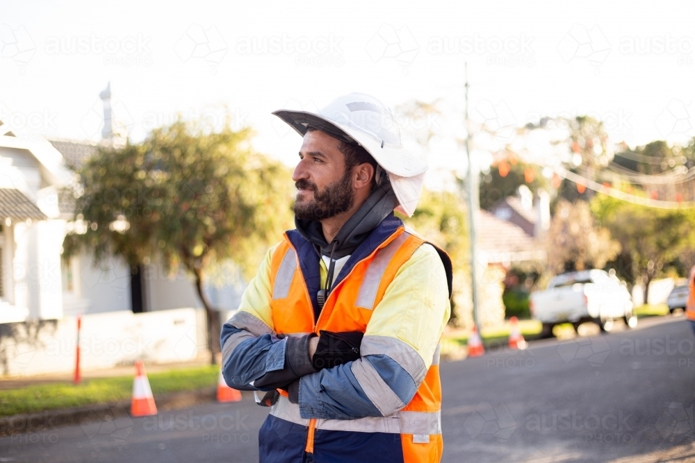 Man road worker with beard wearing white hat looking away while crossing his arms - Australian Stock Image