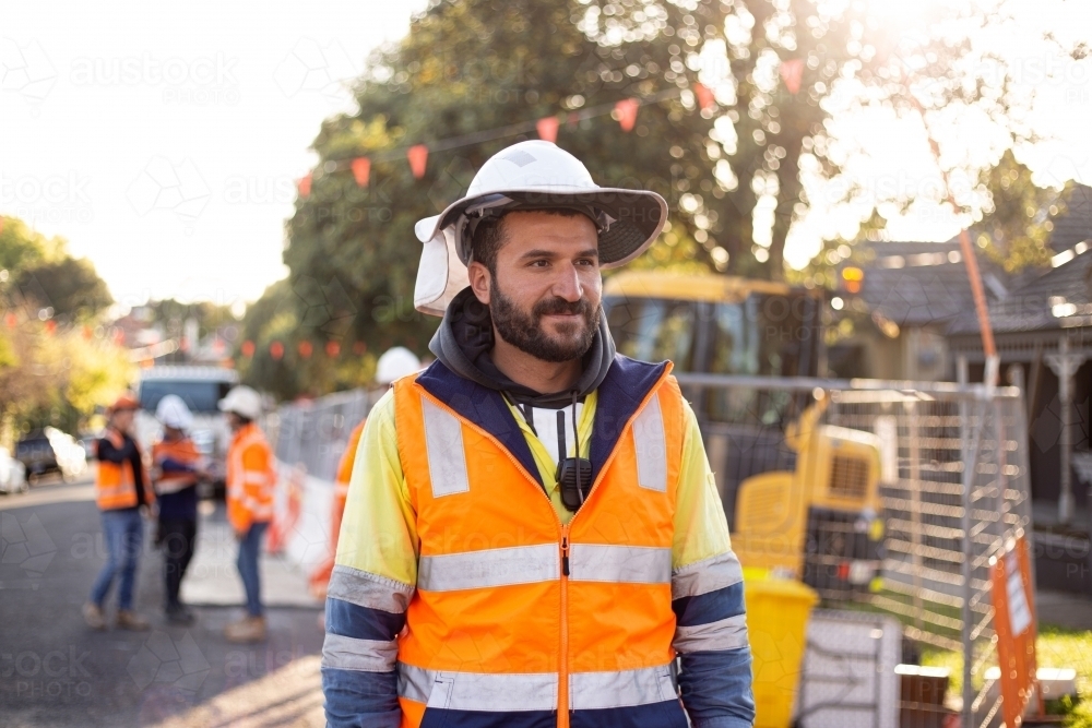 man road worker with beard wearing white hat with yellow and orange high-vis jacket doing roadwork - Australian Stock Image