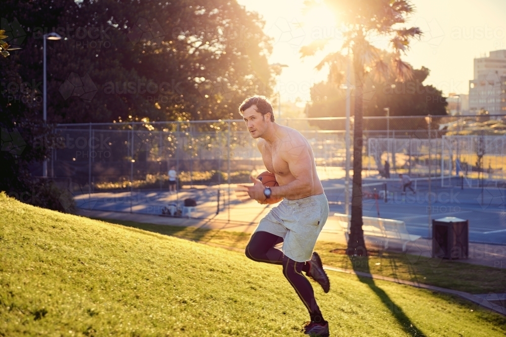 Man running up hill in the early morning with basketball - Australian Stock Image