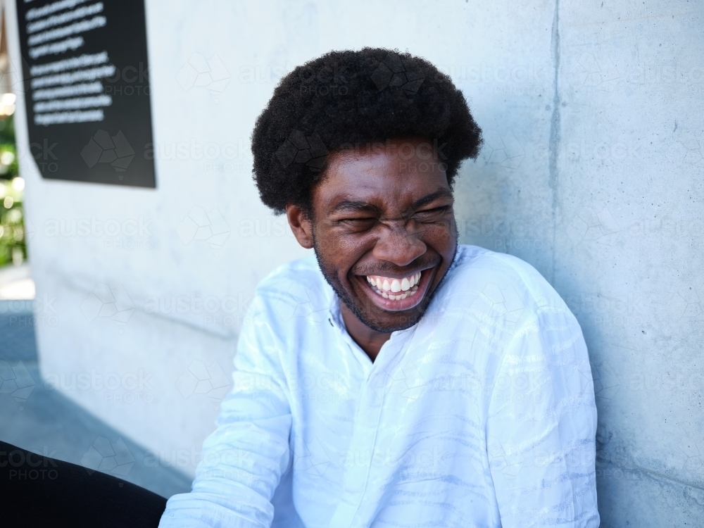 Man sitting against a concrete wall laughing - Australian Stock Image