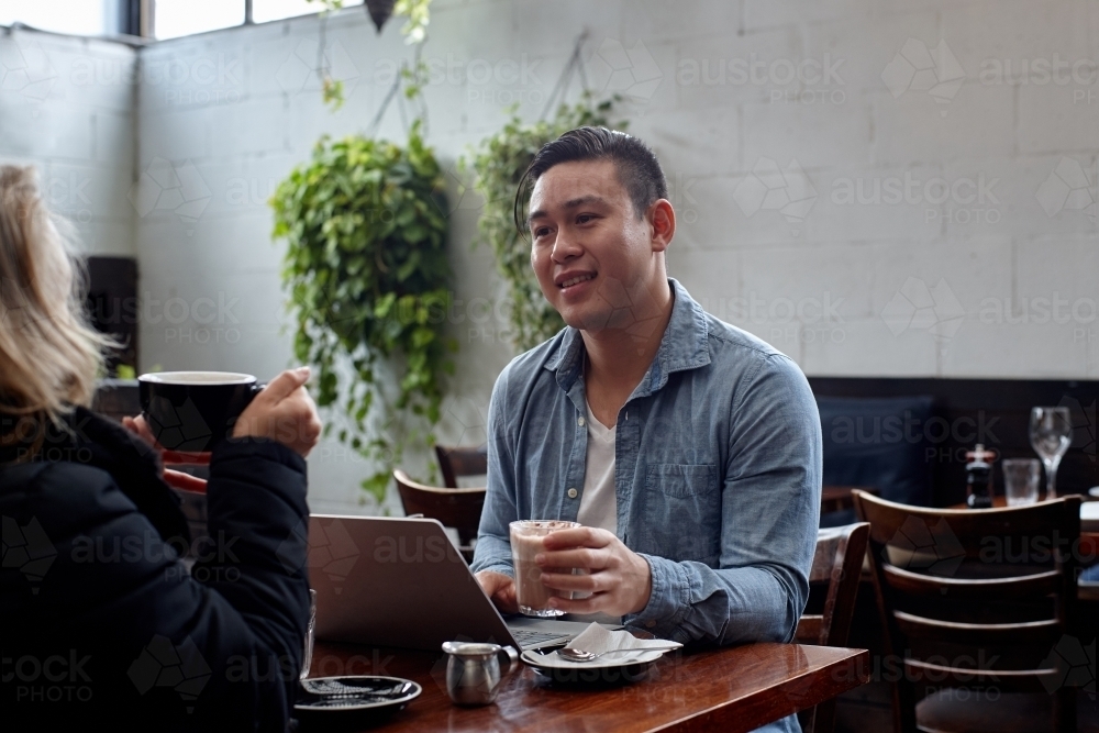 Man sitting at table at restaurant talking with friend - Australian Stock Image