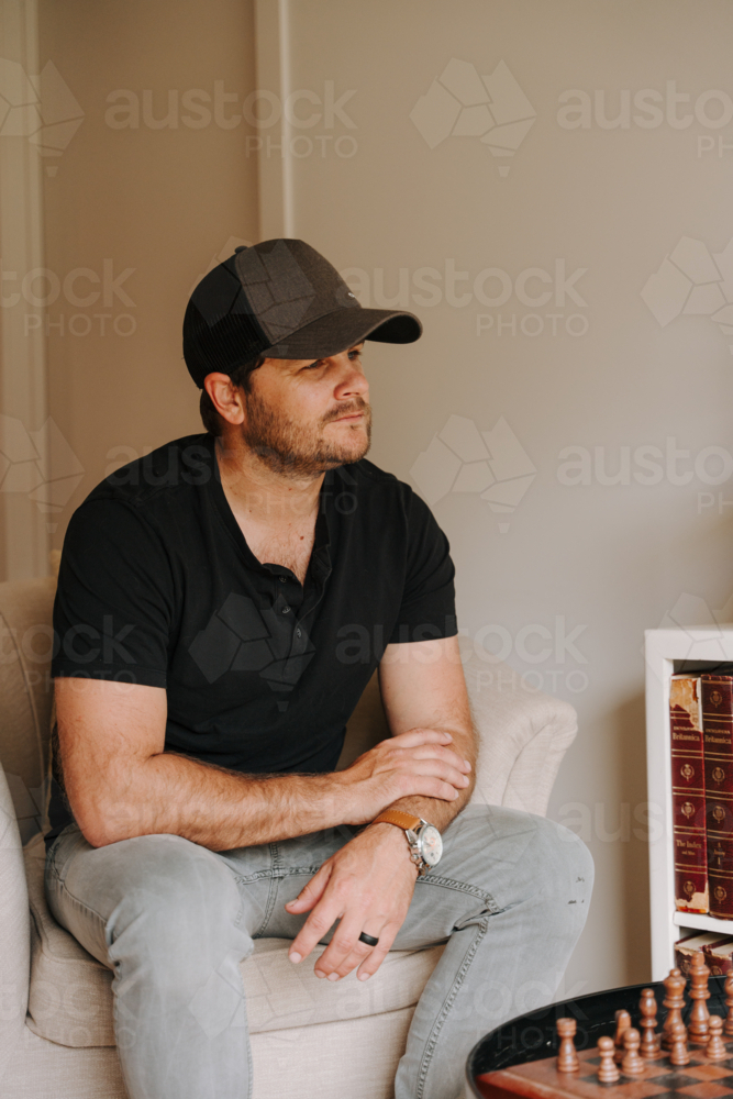 Man sitting on chair at home looking off-camera - Australian Stock Image