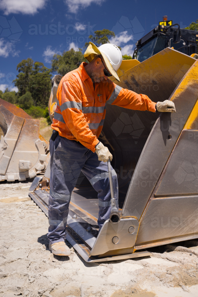Man standing inside the bucket of a payloader. - Australian Stock Image