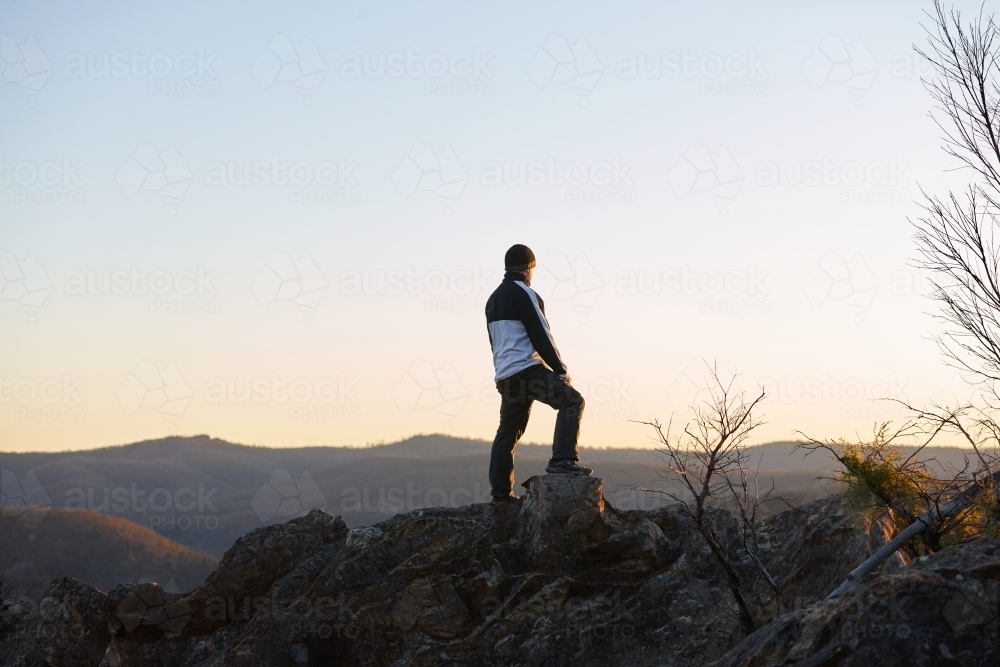 Man standing looking out over mountains on sunset - Australian Stock Image