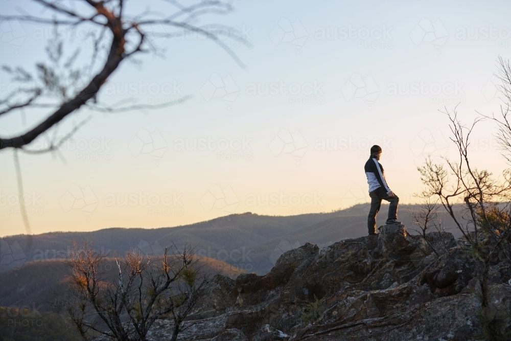 Man standing looking out over mountains on sunset - Australian Stock Image