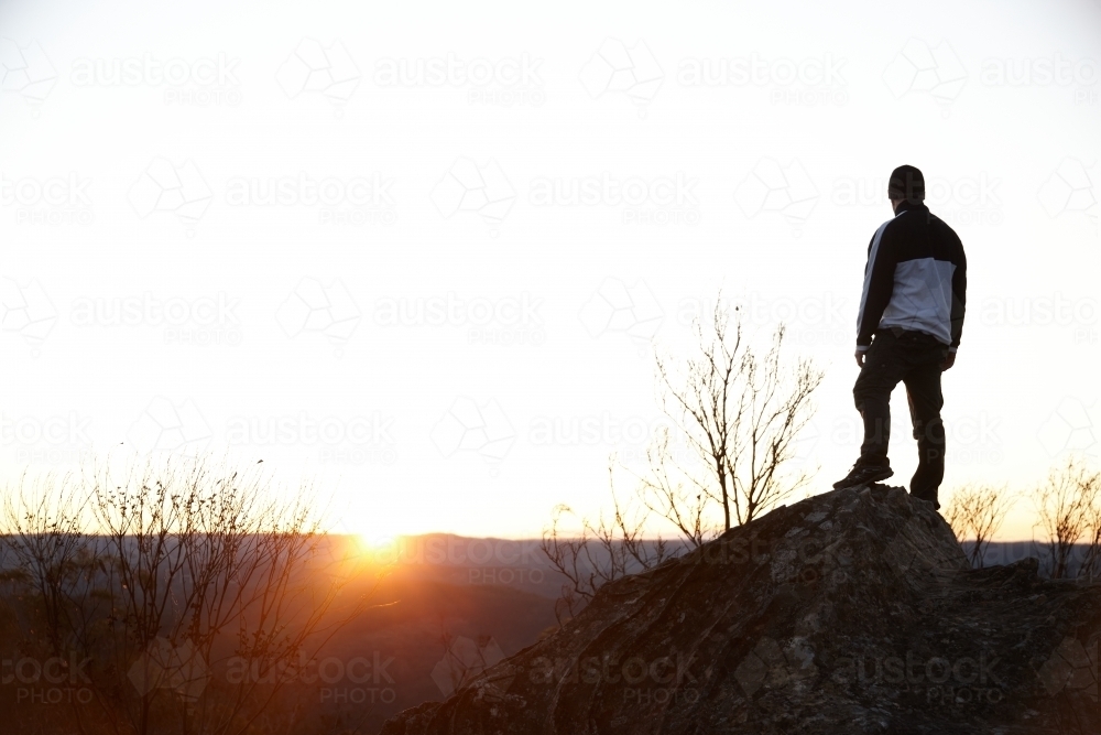 Man standing looking out over mountains on sunset - Australian Stock Image