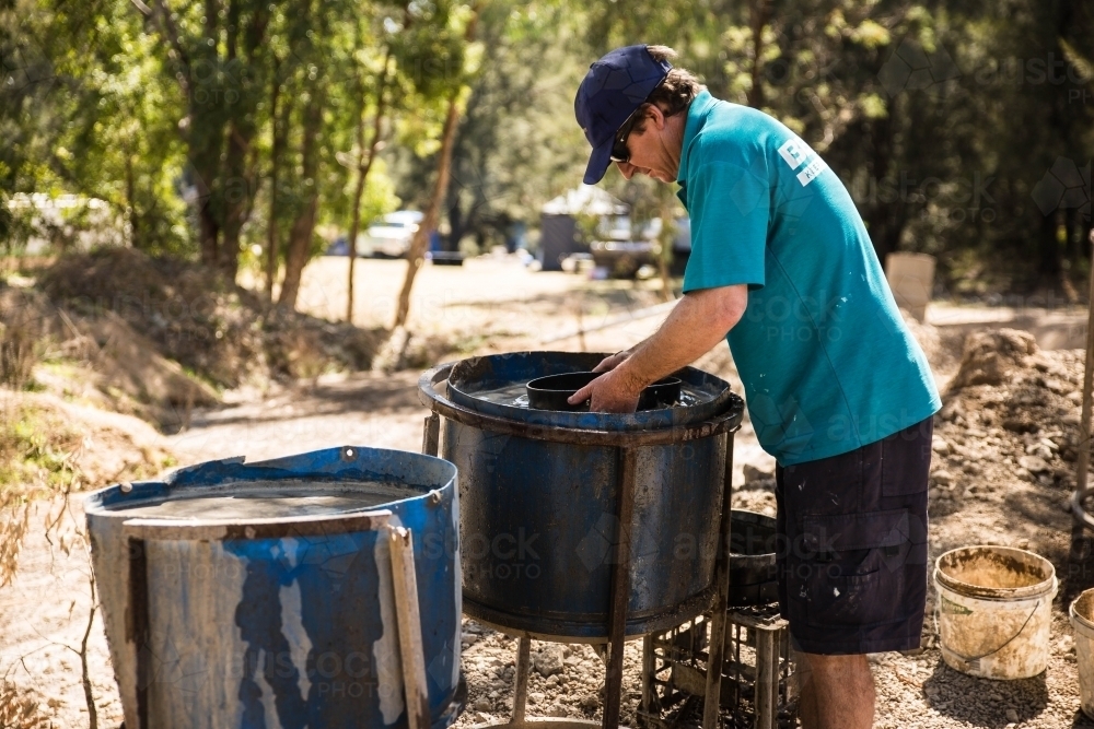 Man standing over fossicking drums of water with sieve - Australian Stock Image