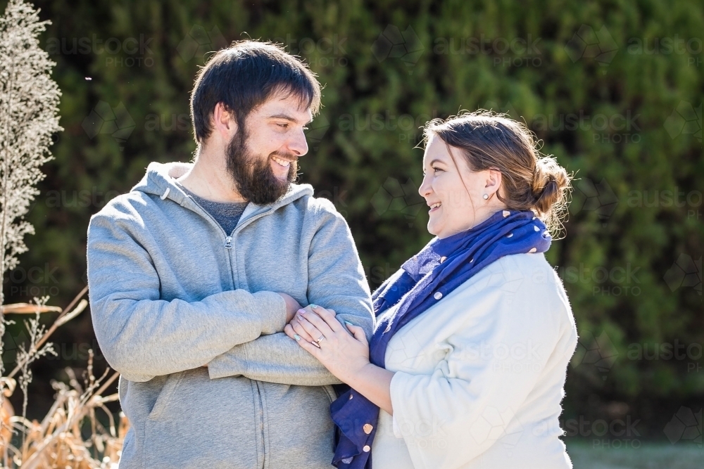 Man standing with arms crossed looking at wife smiling - Australian Stock Image