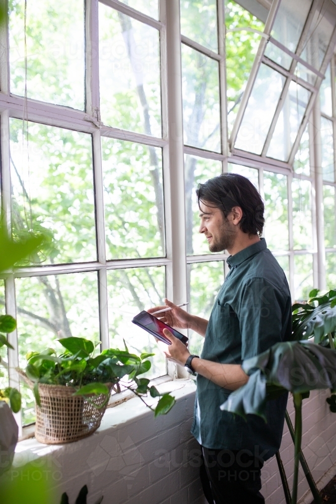 Man standing with device looking through windows - Australian Stock Image