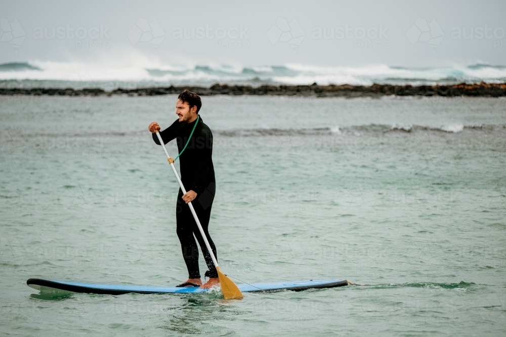 Man standup paddle boarding in the sea. - Australian Stock Image
