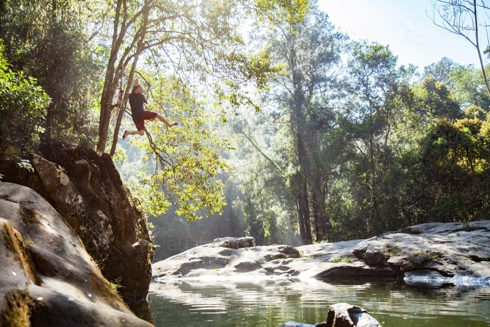 Man swinging out over river on rope - Australian Stock Image