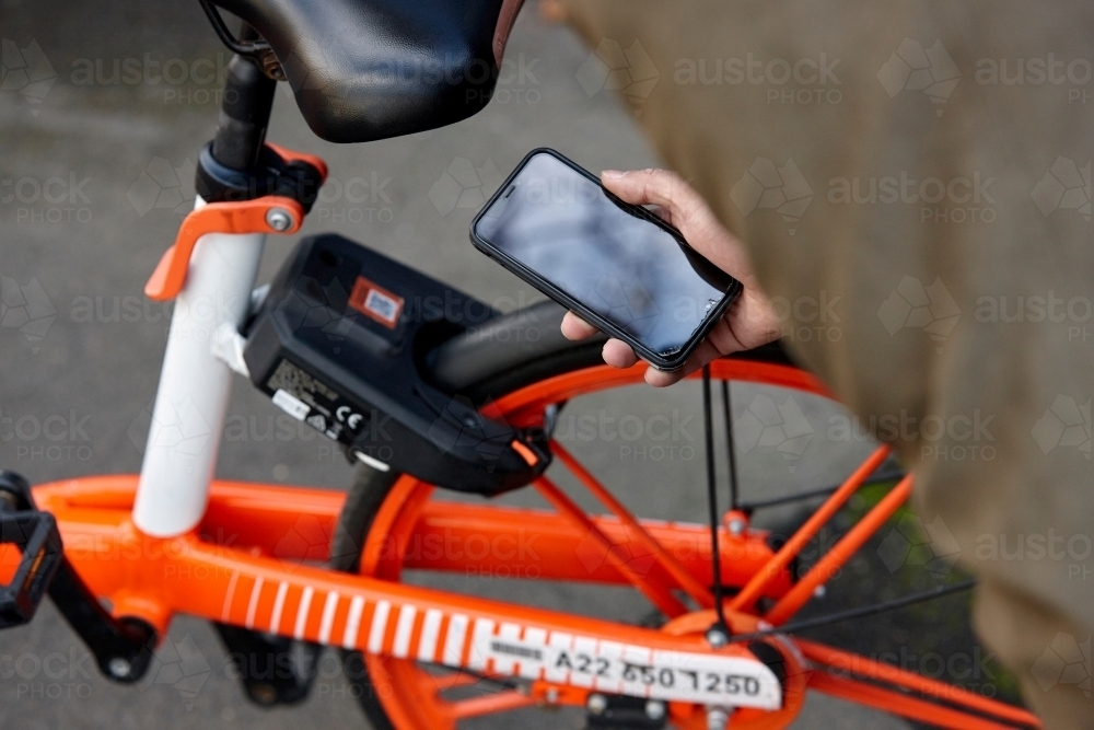 Man using mobile phone to unlock two-wheeled bike-sharing vehicle in city - Australian Stock Image