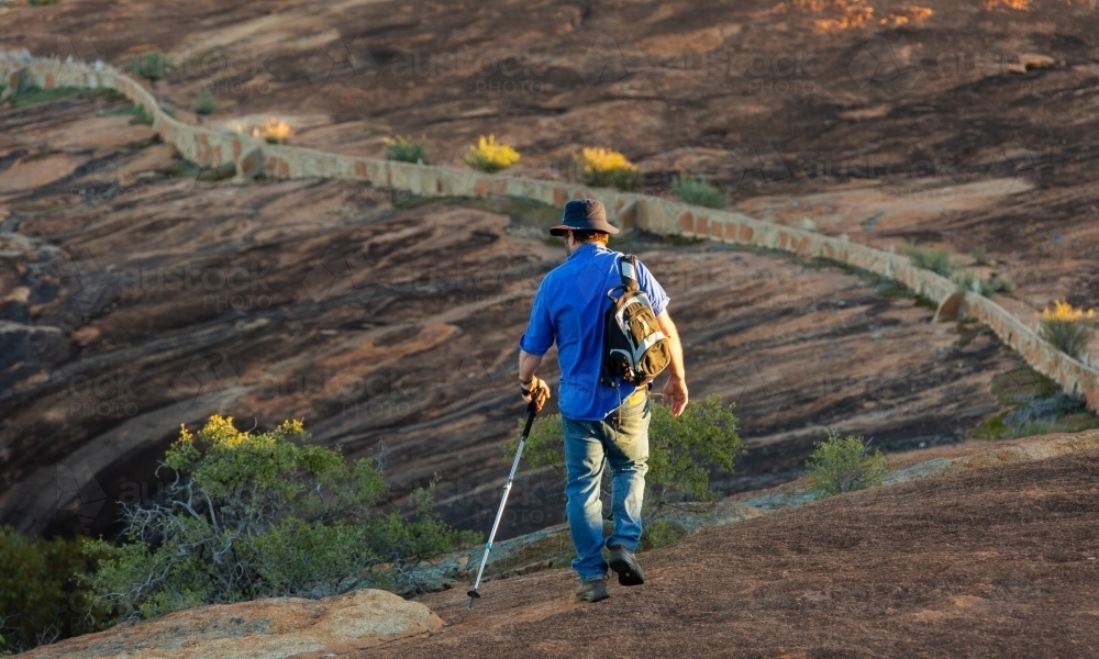 man walking away across a granite rock with historic water catchment wall - Australian Stock Image