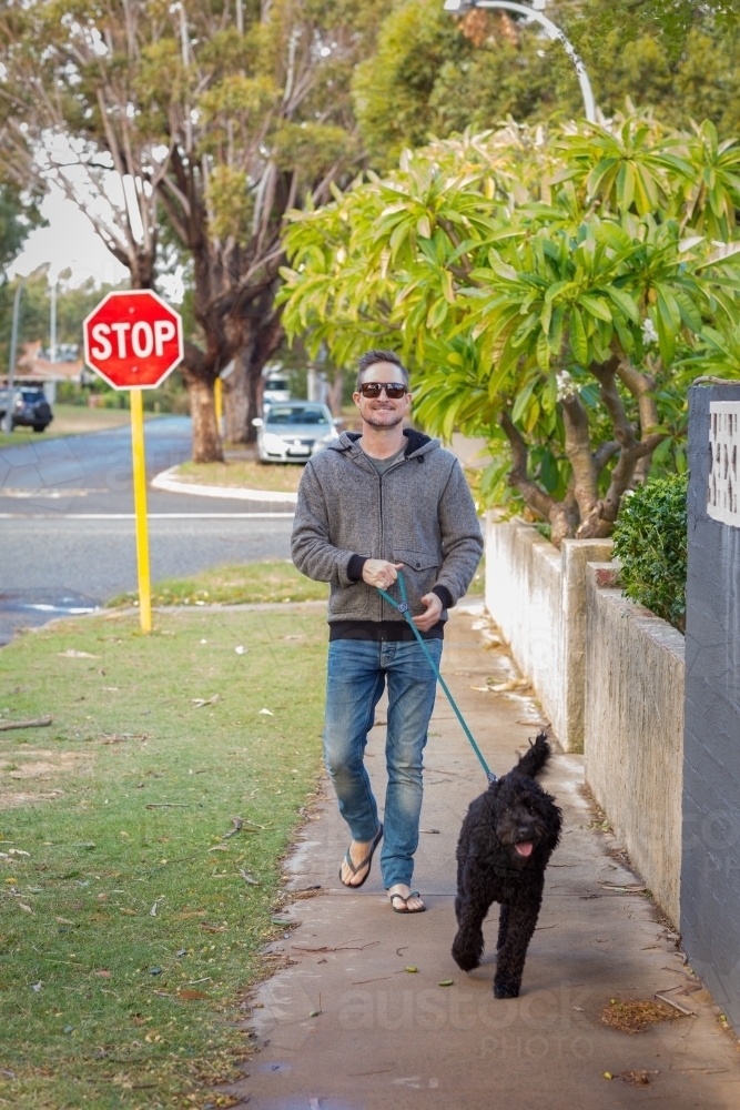 Man walking black dog along suburban street - Australian Stock Image