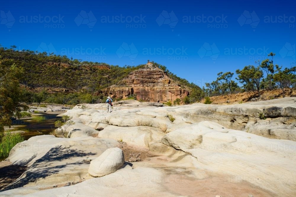 Man walking in a gorge landscape towards rock formation - Australian Stock Image