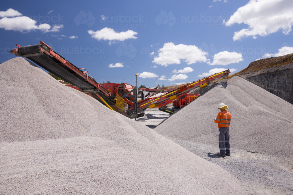 Man walking in between piles of aggregates near the crusher. - Australian Stock Image