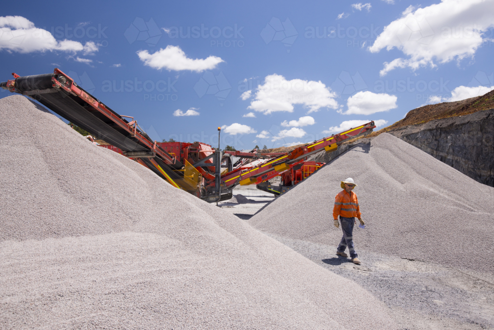 Man walking in between piles of aggregates near the crusher. - Australian Stock Image