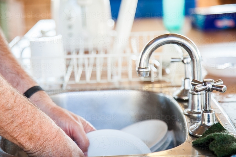 Man washing up plates in sink - Australian Stock Image