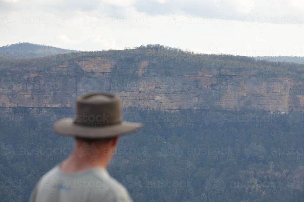 Man wearing Akubra hat looking out over mountain range - Australian Stock Image