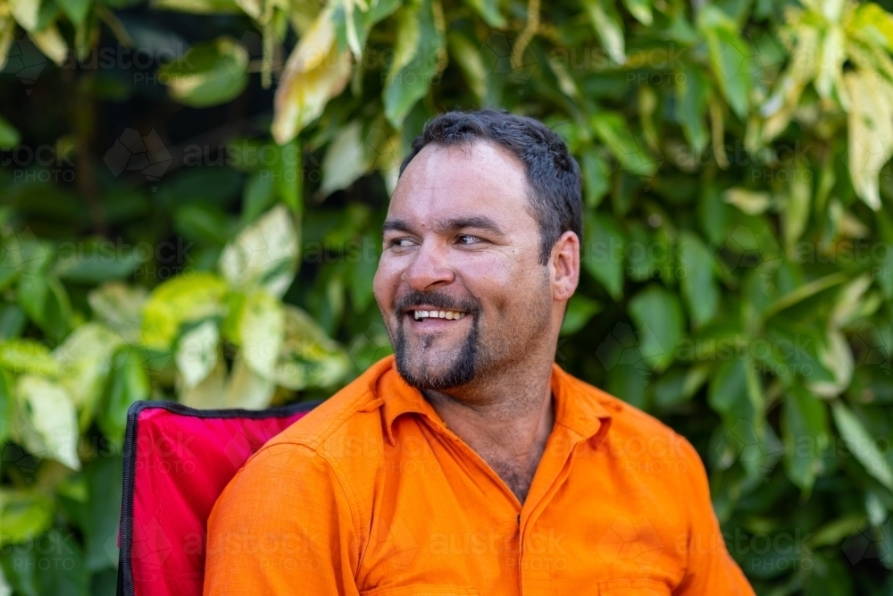 man wearing orange looking away outside with green leafy background - Australian Stock Image