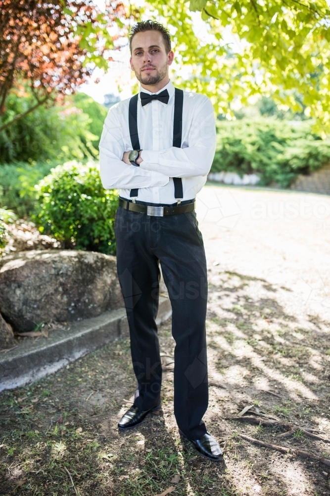 Man wearing suit standing with arms crossed in garden - Australian Stock Image