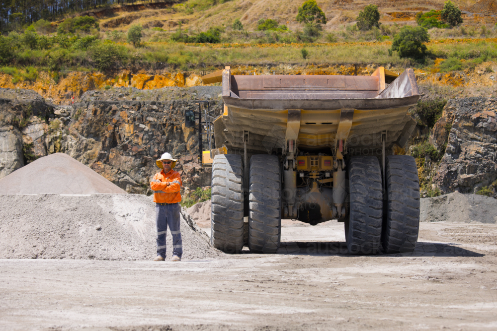 Man with arms crossed standing behind the hauler truck with massive wheels. - Australian Stock Image