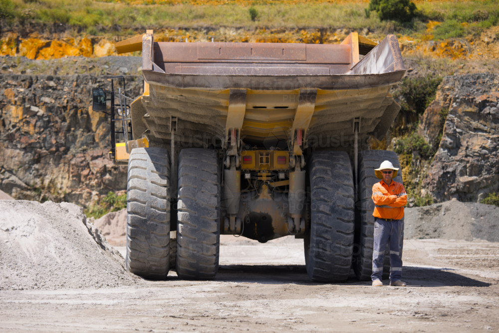 Man with arms crossed standing behind the hauler truck with massive wheels. - Australian Stock Image