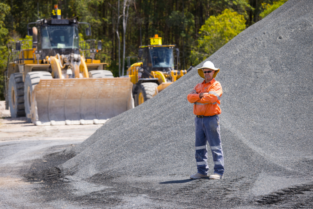 Man with arms crossed standing in between aggregate piles. - Australian Stock Image