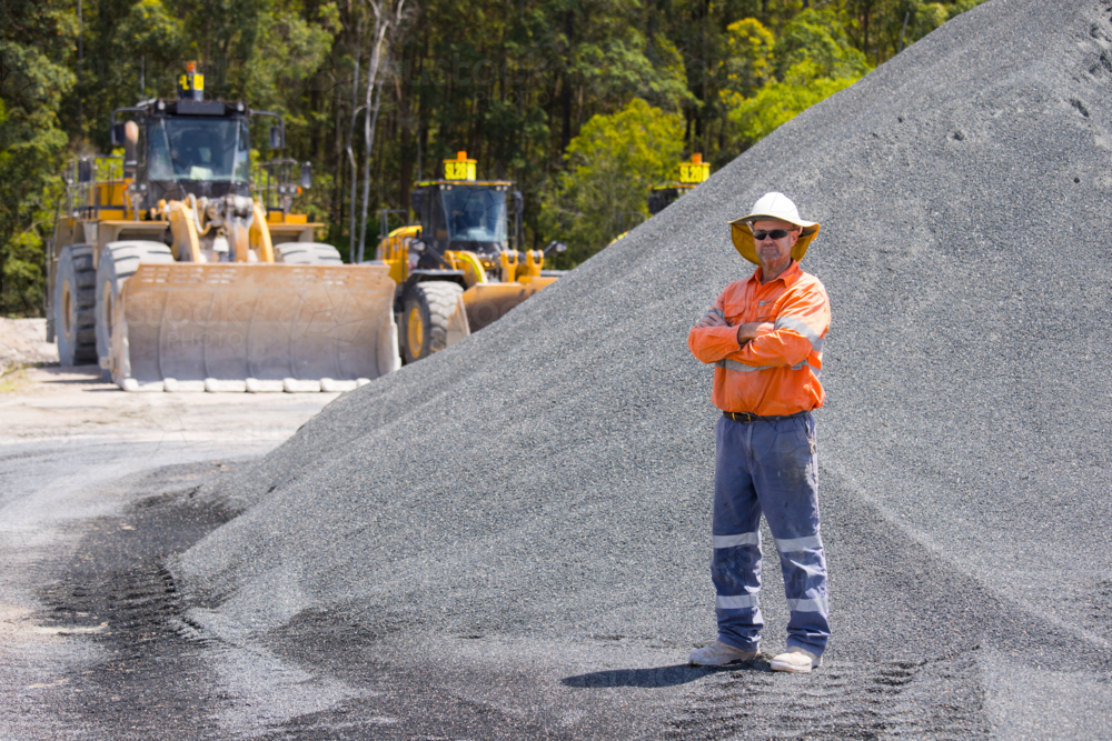 Man with arms crossed standing in between aggregate piles. - Australian Stock Image