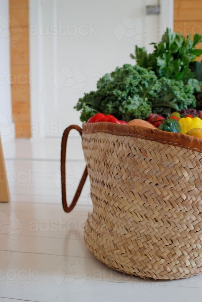 Market basket with fruit and vegetables on white floorboards - Australian Stock Image