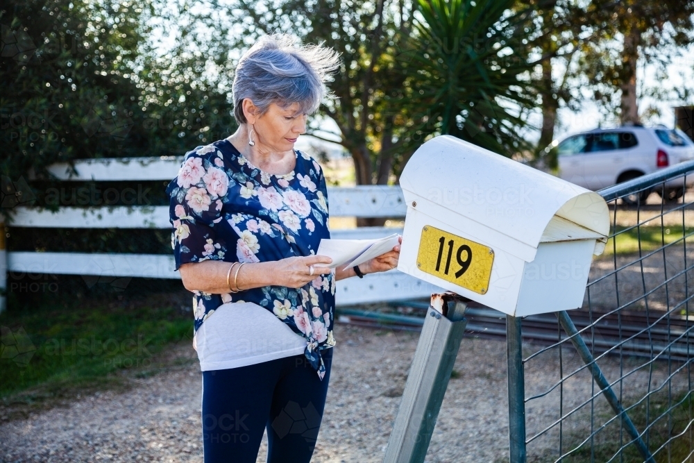 Mature aged woman checking her mailbox for letters - Australian Stock Image