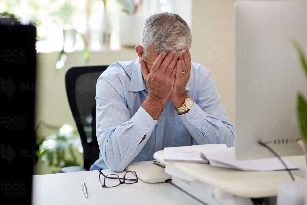 Mature business man sitting at a desk in a studio, thinking, worried - Australian Stock Image