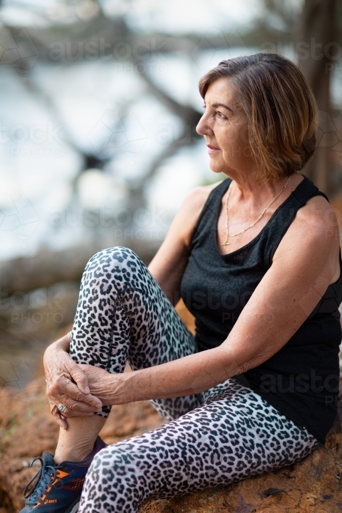 mature lady in activewear sitting in quiet spot by river - Australian Stock Image