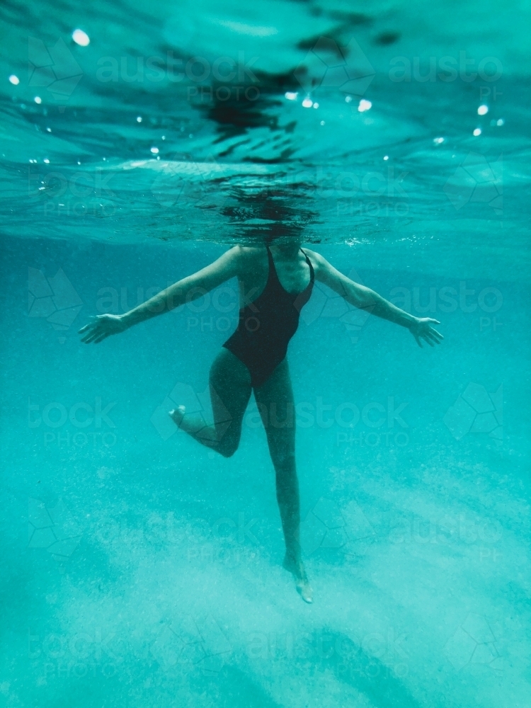 Mature woman's athletic body treading water from underwater perspective in ocean - Australian Stock Image