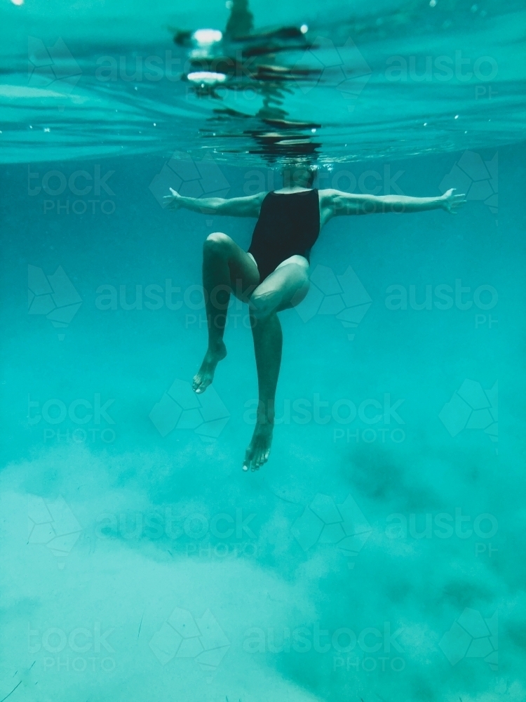 Mature woman's athletic body treading water from underwater perspective in ocean - Australian Stock Image